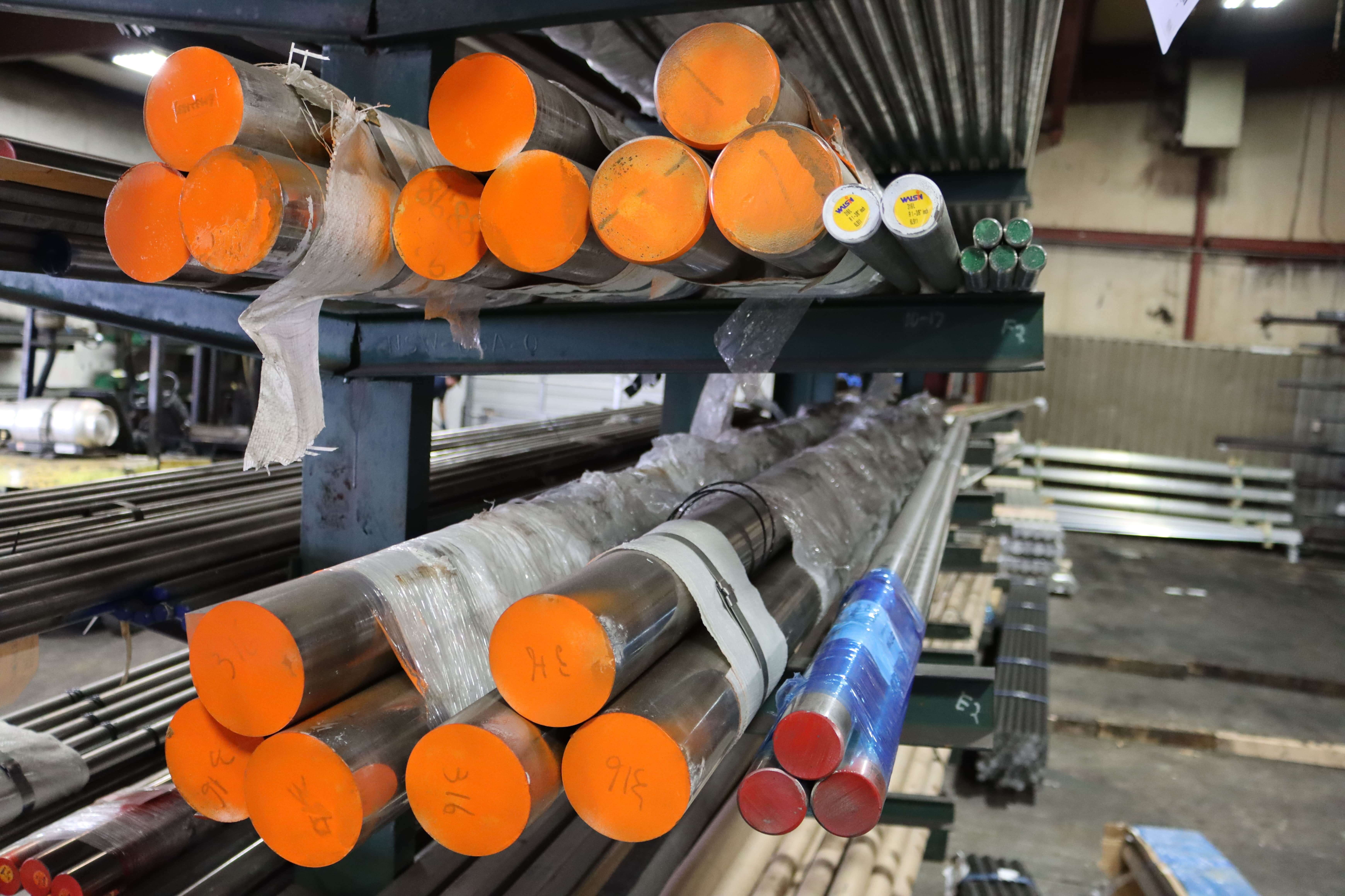 Metal Rods Stored in Industrial Warehouse Storage rack with various metal rods wrapped in plastic, featuring bright orange and red caps in an industrial warehouse.