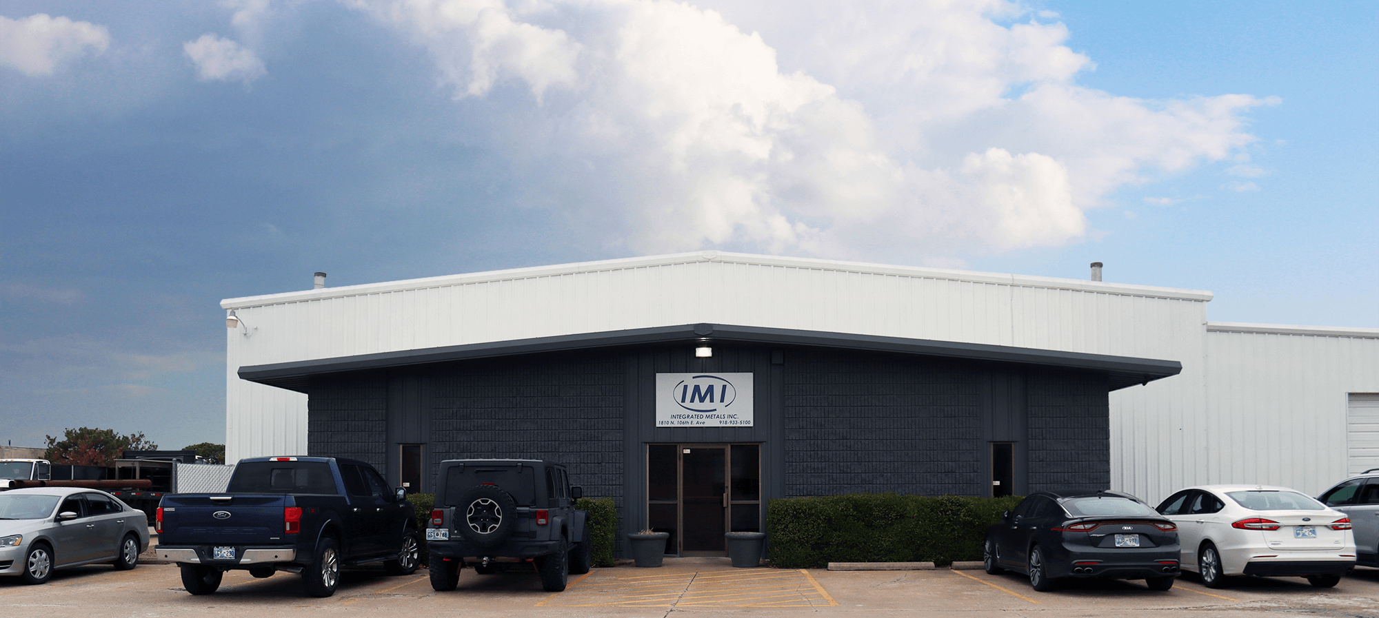 Integrated Metals Inc. Building Front View Front view of the Integrated Metals Inc. (IMI) building with a parking lot, cars, and cloudy sky overhead